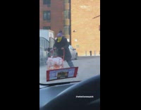 Woman pushes orange cart on rollerskates down sidewalk
