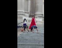 Two guys do ab exercise while woman in background models at courthouse