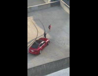 Woman carries flower pictures man in front of red car