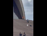 Woman in brown coat crouch pose outside the opera house