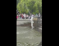 Person covered in white paint wearing arch stands in fountain