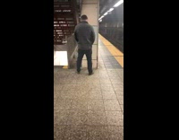 Guy pees on pillar wall in subway station while people pass by