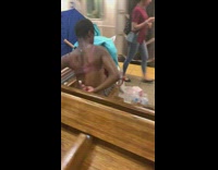 Homeless woman in pink bra brushes her back with a toothbrush sitting on subway station bench