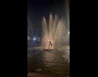 Guy wearing wetsuit leans back on fountain 