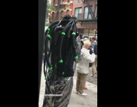 Man with VR headset and green black tube hair metallic shiny outfit on sidewalk