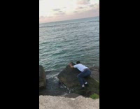 Guy tries to jump on some rocks beach almost slips into water 