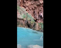 Guy jumps from small cliff near cave 