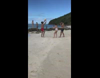 Red shorts guy holds up ball beach 