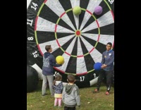 Guy throws blue ball on into giant inflatable velcro dart board at gets bullseye