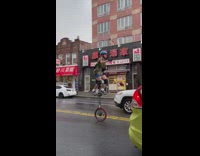 Guy rides on tall unicycle in the rain 