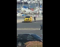 Man in yellow outfit talks beside a yellow car