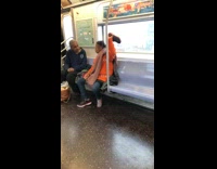 Woman orange jacket takes off shoe and holds it in the air on subway train