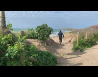 Collab Kook Of The Day - Guy wearing wetsuit carries white surfboard beach