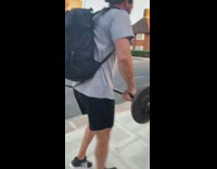 Guy walks down sidewalk lifts barbell 