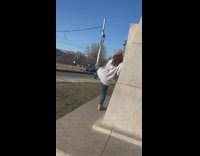 Woman in white coat raises feet beside the statue