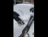 Boy makes snow angels on top of snow covered car 