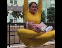 Woman yellow outfit holding up baby with legs from metal bar