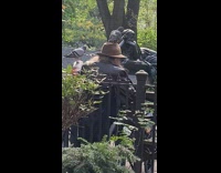 Man brown hat leather jacket sits on park bench with pigeon on his head