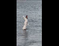 Woman in angel costume poses at the beach at sunset