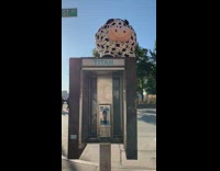 Big toy plush cow sits on top of payphone stall 