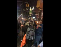 Guy carries snake on shoulder, iguana on head, and green parrot bird on backpack handle 