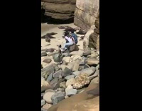 Couple sits on a rock at the beach shore