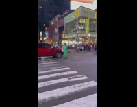 Guy in green jump suit at busy intersection dancing in between cars