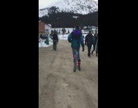 Guy walks down concrete pavement wearing skis 