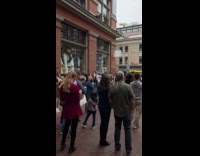Woman sells product behind crowd on sidewalk
