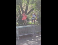 Guy in pink and lady in white dance and yell on guard rails 