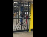 Man black shirt fights guy red pants in subway station behind turnstile gates
