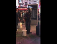 Shirtless guy in scary mask and black cape does resistance band bicep curl on the sidewalk