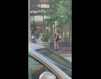 Woman in black dress with a handbag poses on the sidewalk