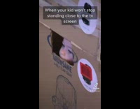 Little kid inside of box with hole to watch tv 