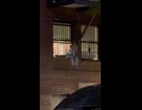 Kid watching street sitting on outward window grills 