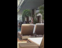 Woman in cyan bikini poses beside a plant by the pool