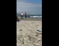 Guy looks down at phone beach sand 