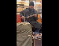 Man performs on subway strumming on guitar