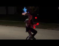 Boy clown costume juggles ball on unicycle