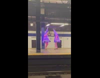 Two ladies wearing purple christmas trees dance 