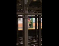 Guy lights a cigarette and smokes while facing green pillar in subway station