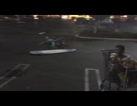 Two guys crash into each other on shopping carts while holding surfboards in parking lot