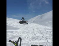 Person does a flip on a snowmobile in snowy mountain