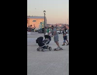 Guy on longboard pushing around a stroller with a baby inside