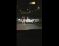 Two girls dance behind white car night