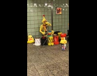 Guy in yellow chicken costume suit blows whistle and plays drums with buckets in subway station