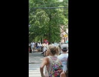Shirtless guy with white jacket tied around waist dances on sidewalk corner on the phone