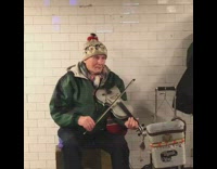 Guy wearing green jacket plays violin at subway station