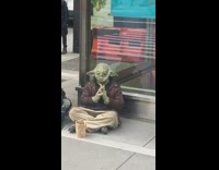 Guy green yoda costume mask sits sidewalk 