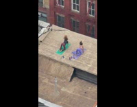 Two women doing a yoga workout on yoga mats on a rooftop building 
